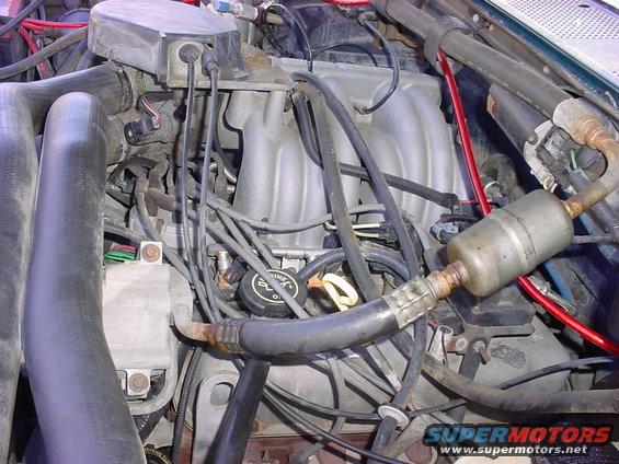 Engine bay with hoses, wires, and intake manifold visible. Oil cap reads 'Ford Motorcraft'