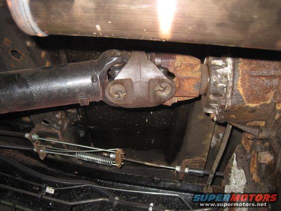 Close-up of a driveshaft connected to a rusty transmission housing, with cables and springs visible