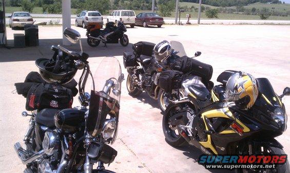 Several motorcycles parked at a gas station, some with luggage attached