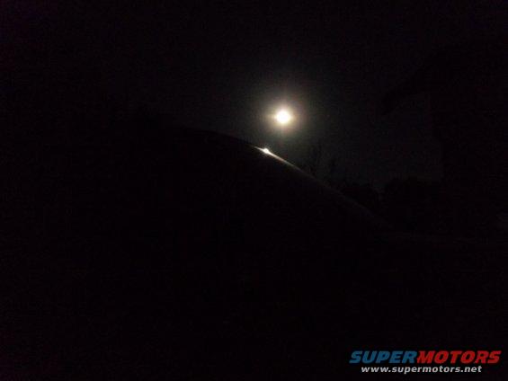 Dark car roofline under moonlight, with a bright light source reflecting off the surface