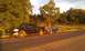 1991 Ford Festiva - A black pickup truck tows a small blue hatchback along a rural road during golden hour.