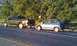 1991 Ford Festiva - A blue 1991 Ford Festiva is being towed by a dark-colored pickup truck on the side of a road.