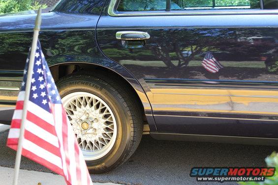 1999 Ford Crown Victoria side view with American flag on pole and reflected in door