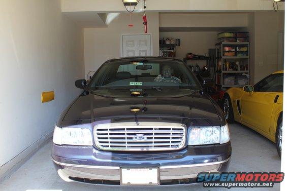 Dark sedan with chrome grille and a driver inside, parked in a garage next to a yellow sports car