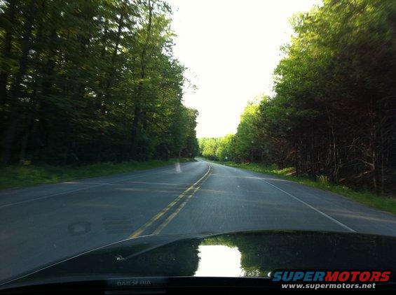 Driving down a two-lane road surrounded by trees. The sun is bright overhead