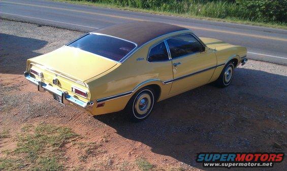 Yellow coupe with a brown roof parked on a gravel shoulder next to a road. It has a chrome bumper and trim