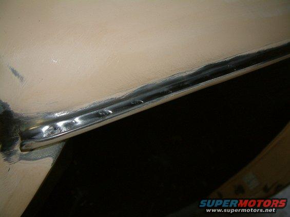 Close-up of a chrome trim piece on a light-colored vehicle body panel, showing some imperfections