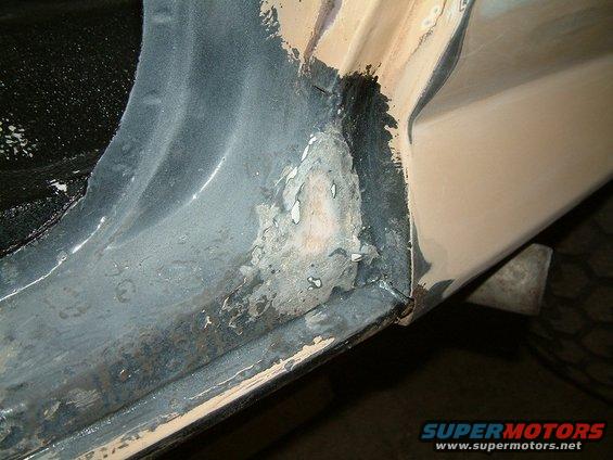 Close-up of rust damage on a vehicle's door frame, showing exposed metal and primer