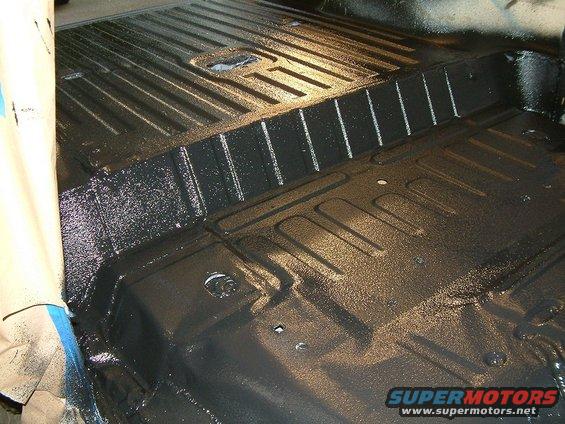 Vehicle floor pan being coated with black undercoating. Ribbed texture visible