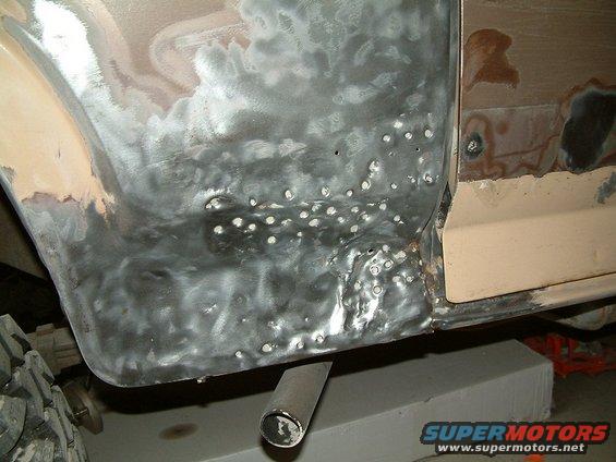 Vehicle body panel with extensive rust repair, showing bare metal, primer, and weld spots