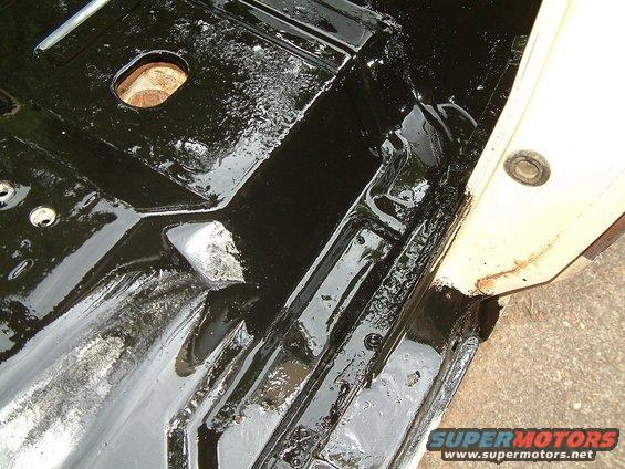 Black undercoating on vehicle floor pan with visible rust and a circular opening