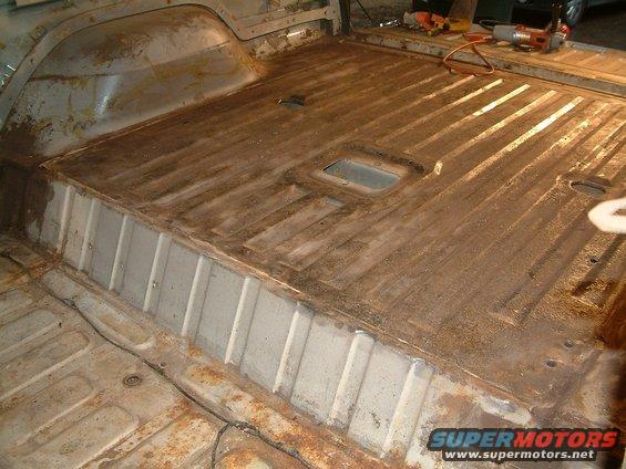Interior of a vehicle with floor stripped down to metal, showing rust and some repair work