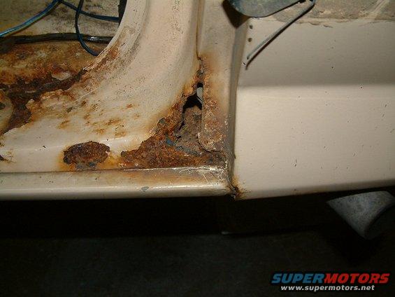 Close-up of heavily rusted beige vehicle door frame with exposed metal and wiring