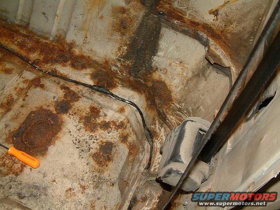 Orange handled screwdriver on rusted metal floor pan with black wiring and a black component