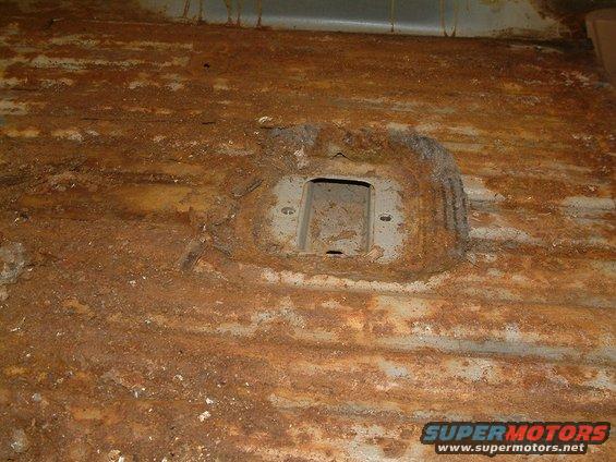 Rusted interior floor pan with a metal bracket and mounting holes
