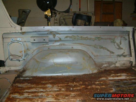 Interior of a heavily rusted truck bed, showing wheel well and floor