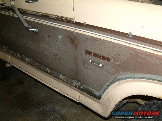 Side view of a 1983 Ford Bronco with woodgrain paneling and chrome trim. The paint is faded and there are some dents