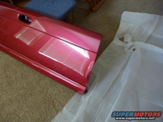 Red vehicle door with black handle, resting on carpet next to white protective sheeting