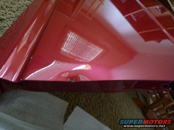 Red car fender with reflection of a ceiling light and wooden chairs