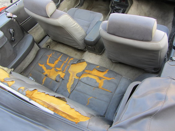 Torn gray interior seats of a convertible with yellow foam exposed