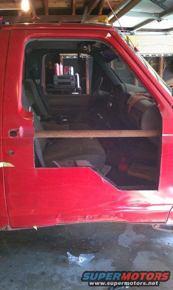 Red truck cab interior with cut-out door, showing seats and dashboard. A wooden bar is across the opening