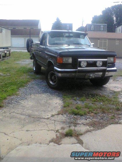 Dark blue Ford F-Series truck with a spare tire mounted on the back, parked on a gravel driveway