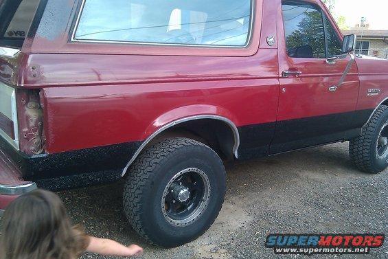 Red and black Ford Bronco, side view. Missing taillight on the left