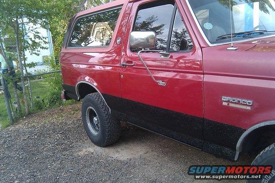 Red Ford Bronco with black lower body trim, side view, showing front fender and door