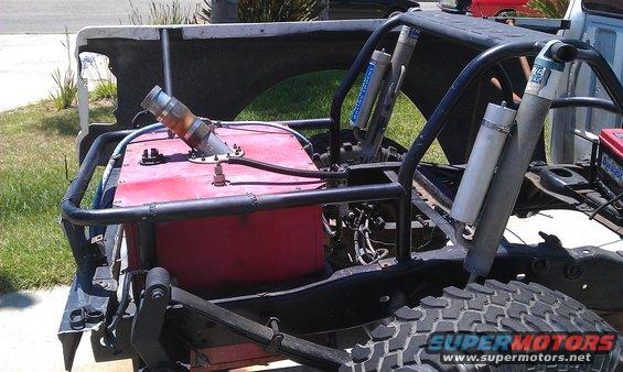 Custom off-road truck chassis showing large red fuel tank, roll cage, and rear shocks. Supermotors.net logo visible