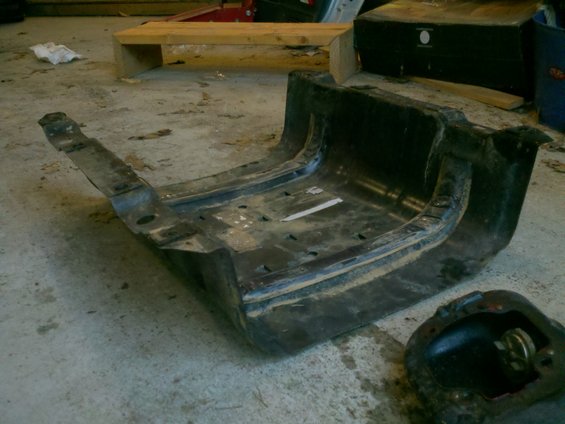 Black metal automotive part with mounting brackets on a concrete floor