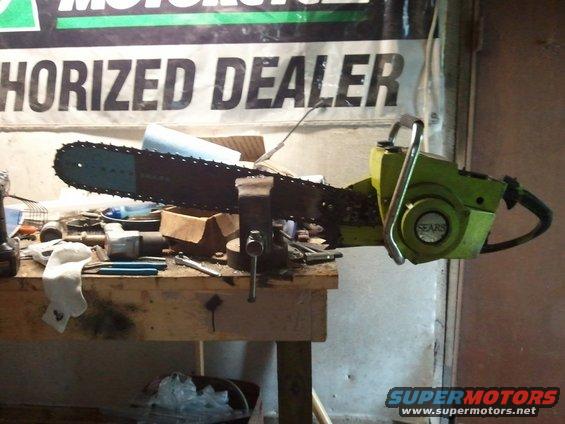 Green Sears chainsaw clamped in a vise on a workbench with tools