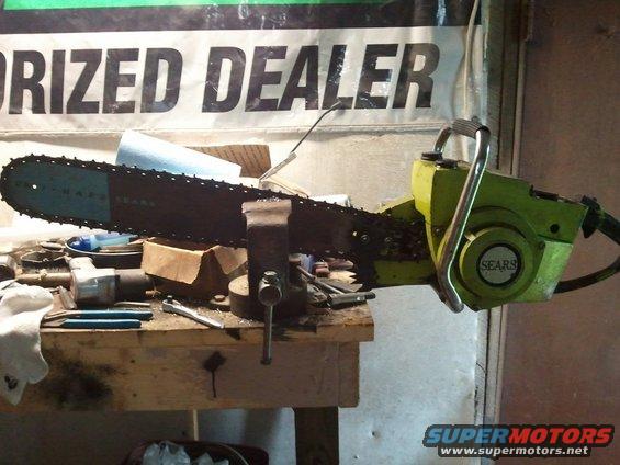 Green Sears chainsaw with a long bar held in a vise on a workbench