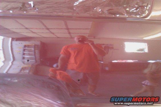 Reflection of a man in an orange shirt in the shiny red paint of a vehicle