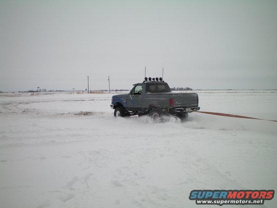Gray pickup truck with blue hood stuck in snow, pulling a tow strap