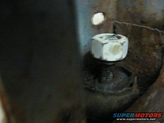 Close-up of a white hex nut on a bolt, with some rust visible on surrounding metal