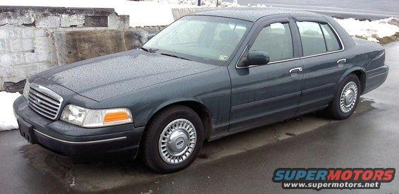Dark green 1998 Ford Crown Victoria sedan, front 3/4 view, wet pavement, snow in background