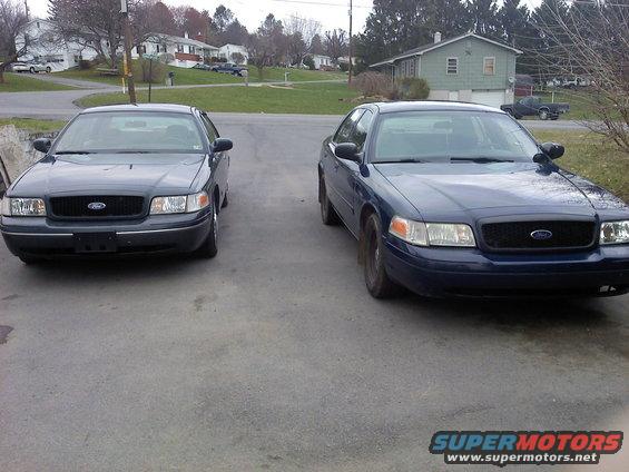 Two dark Ford Crown Victorias, front view, parked on asphalt