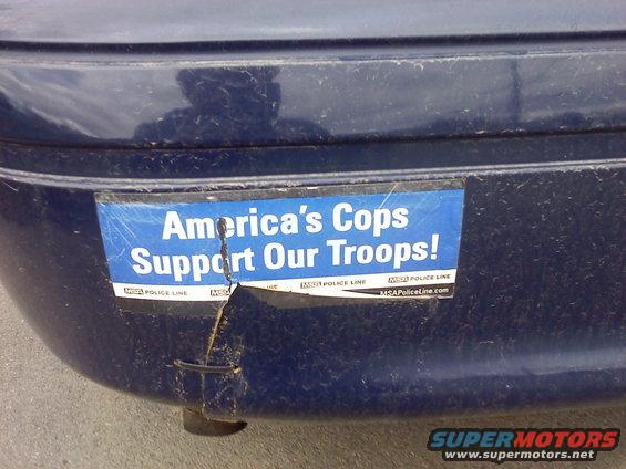 Blue bumper sticker reading "America's Cops Support Our Troops!" on a dark blue car's rear bumper