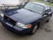 2002 Ford Crown Victoria - A dark blue 2002 Ford Crown Victoria is parked outside on a paved surface, with a picnic table and building in the background.
