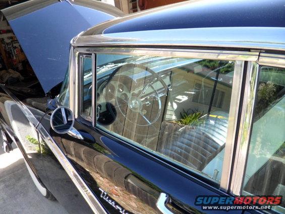 Black 1956 Ford Fairlane interior with chrome steering wheel and quilted seats, seen from the side