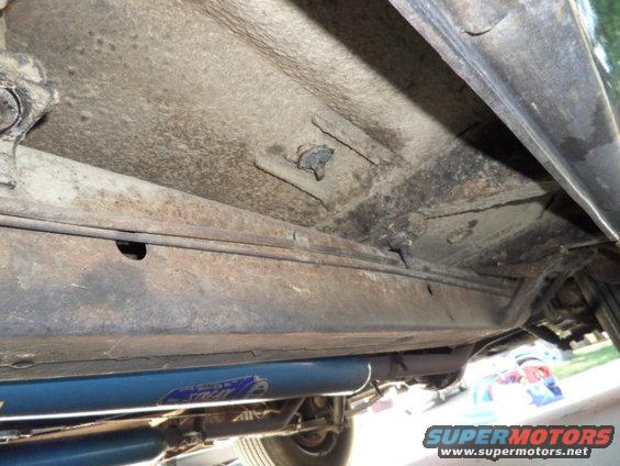 Underside of vehicle showing frame and exhaust system with blue shock absorber