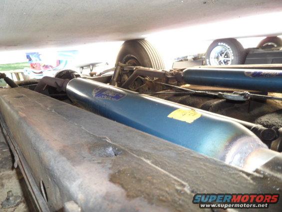 Underside view of a car, showing exhaust pipes and suspension components. A tire is visible in the background