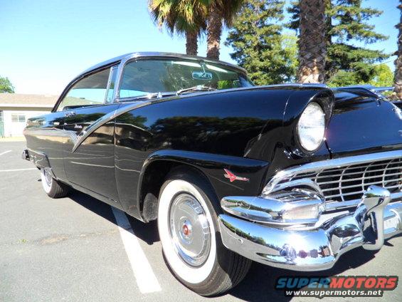 Black 1956 Ford Fairlane coupe with chrome trim and whitewall tires, parked in a lot