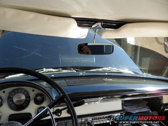 Dashboard view of a 1955 car, showing the steering wheel, instrument cluster, and rearview mirror