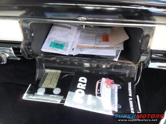 Glove compartment open, showing papers and a 1956 Ford owner's manual