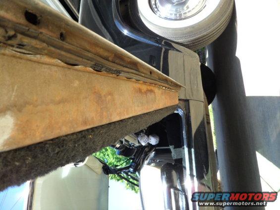 rusted metal trim piece above black car body, chrome wheel visible