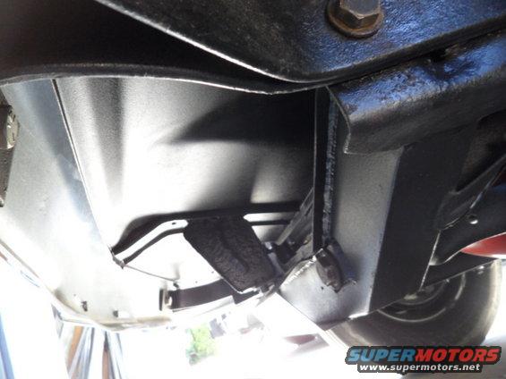 Underside of a vehicle showing frame and suspension components. A tire is partially visible on the right