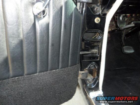 Black pleated door panel with chrome handle and black carpeted lower section. Door jamb and pedals visible