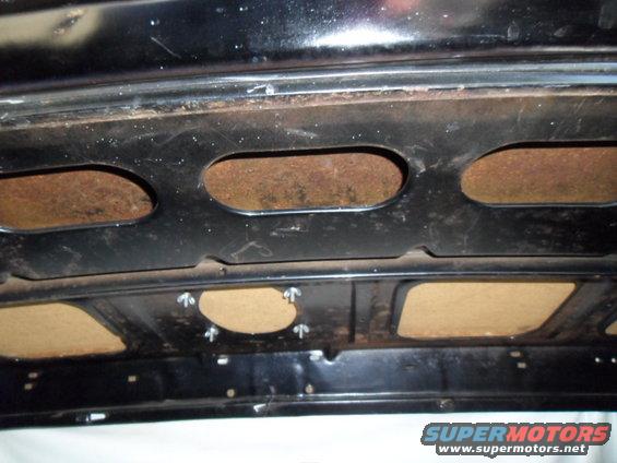 underside of a car hood with rust showing through cutouts and some insulation panels