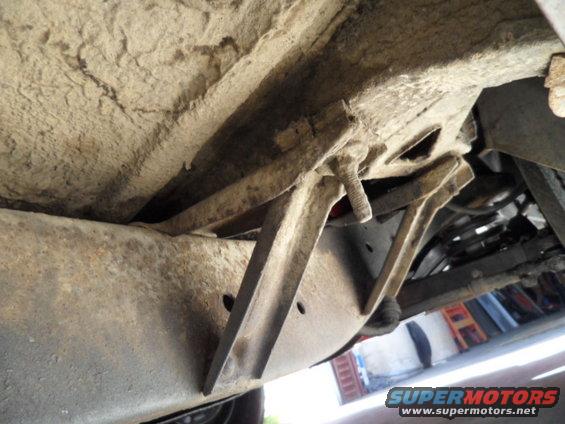 Undercarriage of a vehicle with rusty frame rails and suspension components visible